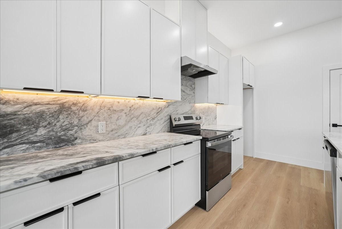 Kitchen with white cabinets, gray-veined stone counters and backsplash, and a stainless steel range.