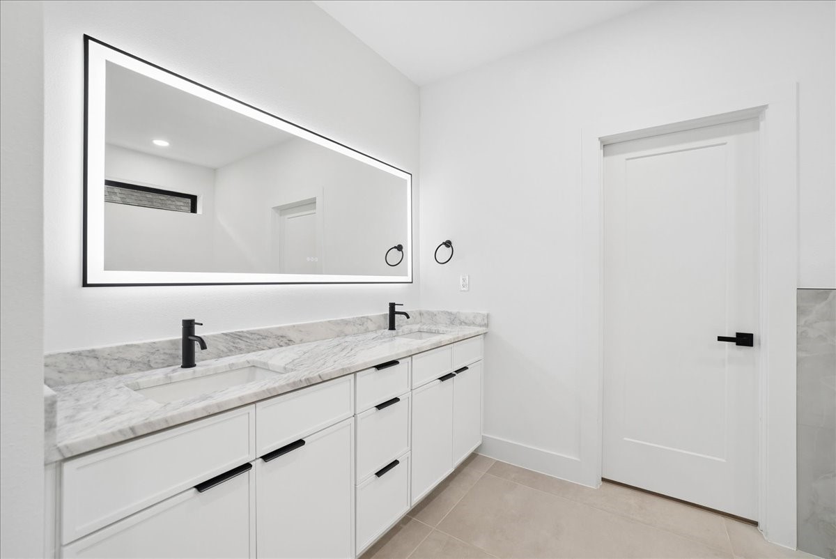 Bathroom with a white double vanity, marble counter, black faucets, and a large framed mirror.