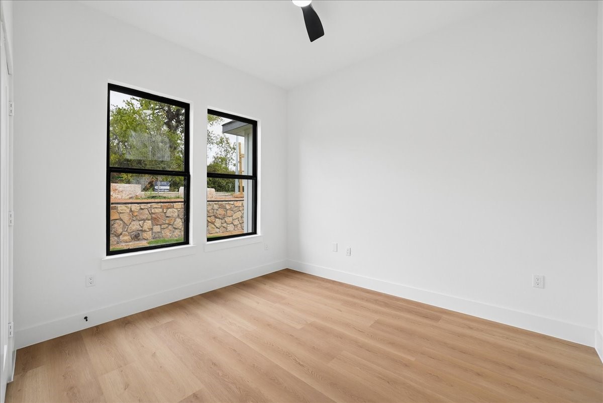 Empty room with light wood floors, white walls, and two black-framed windows.