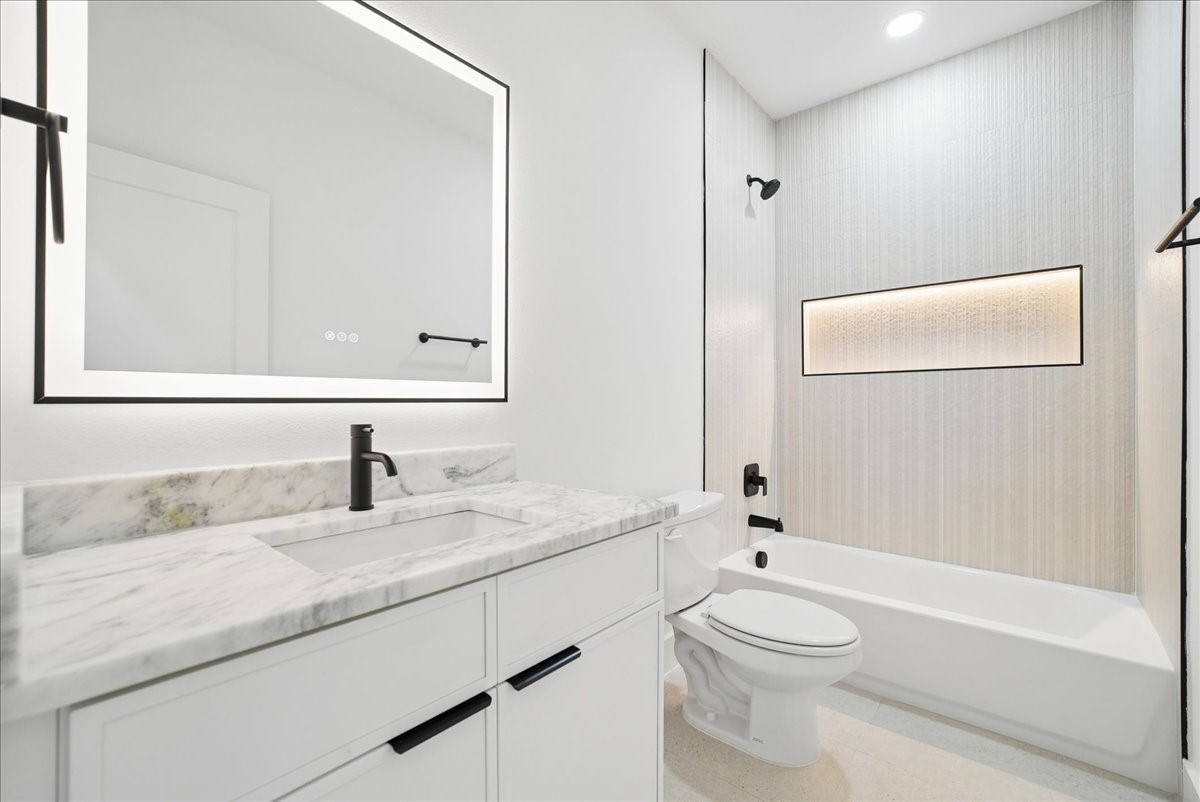 Modern bathroom with a marble vanity, black-framed mirror, and bathtub with black fixtures.