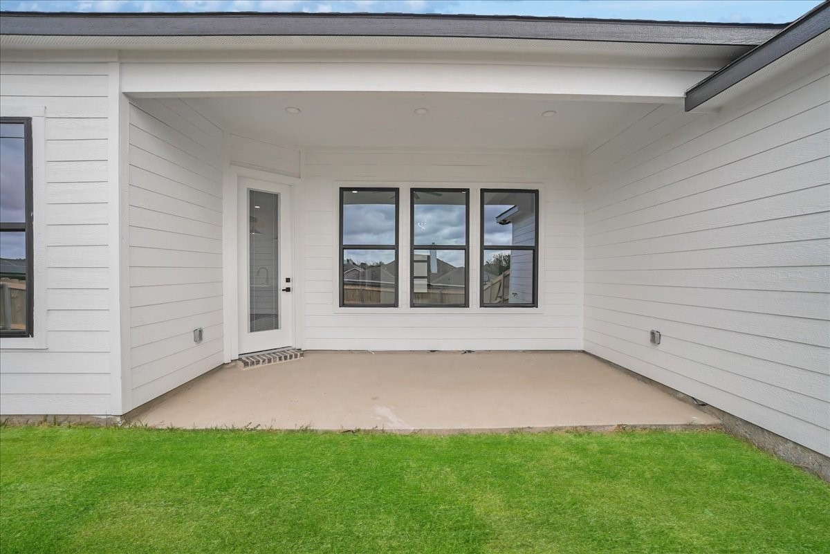 Covered concrete patio with white siding, black-framed windows, and green lawn.
