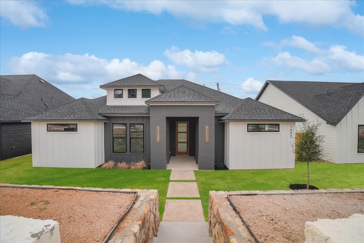 Modern gray-and-white home with a covered entry and stone-bordered walkway.