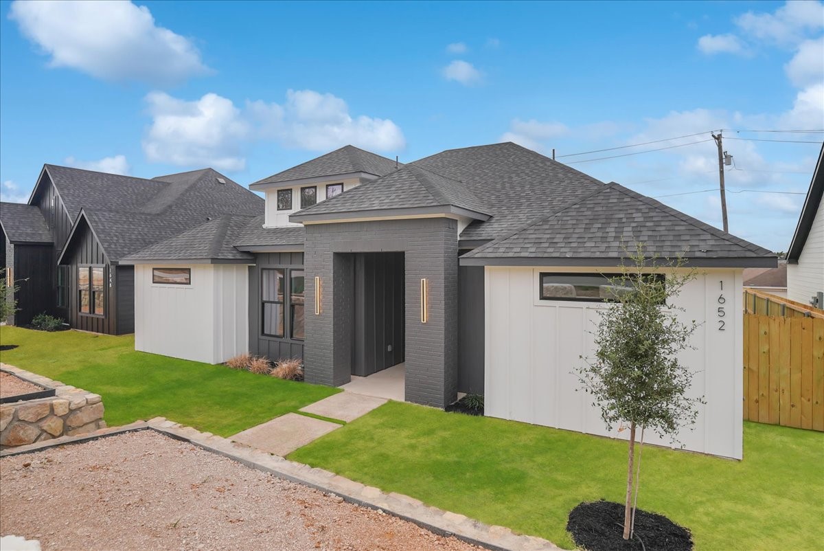 Contemporary home with a dark brick entry, white siding, and landscaped front lawn.