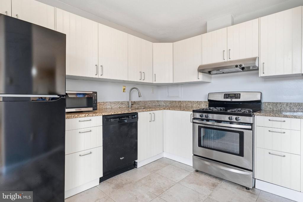 Condo kitchen with white cabinets, speckled countertops, and a stainless steel range.