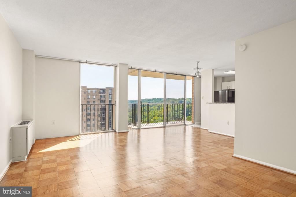 Vacant living room with parquet floors, sliding glass doors, and a balcony overlooking trees.