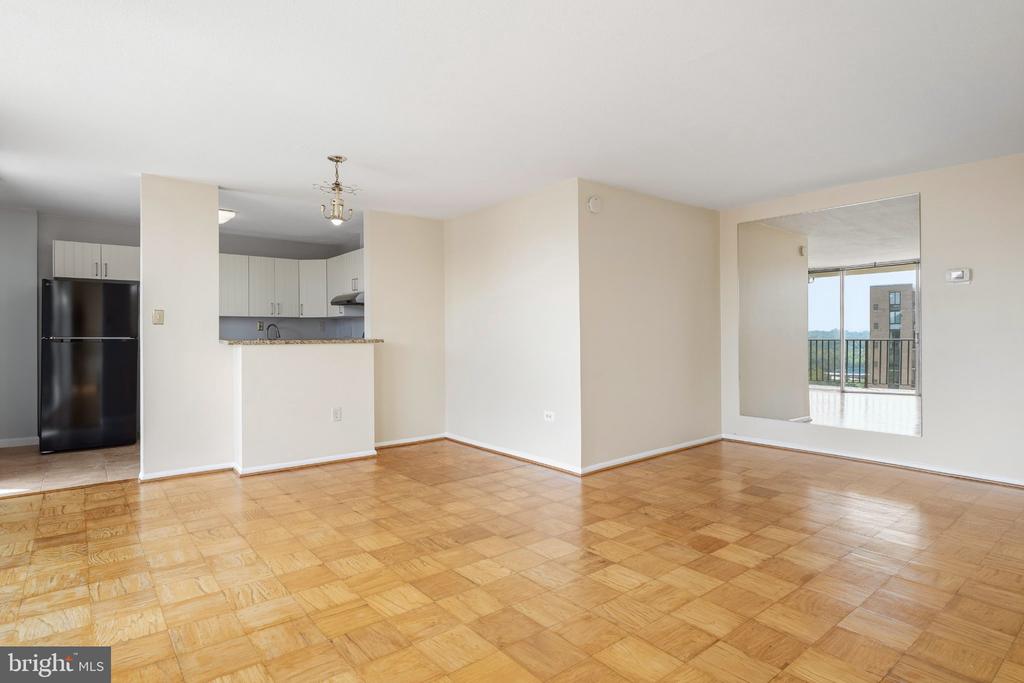Unfurnished condo living area with parquet floors, an open kitchen, and a bright balcony-facing room.