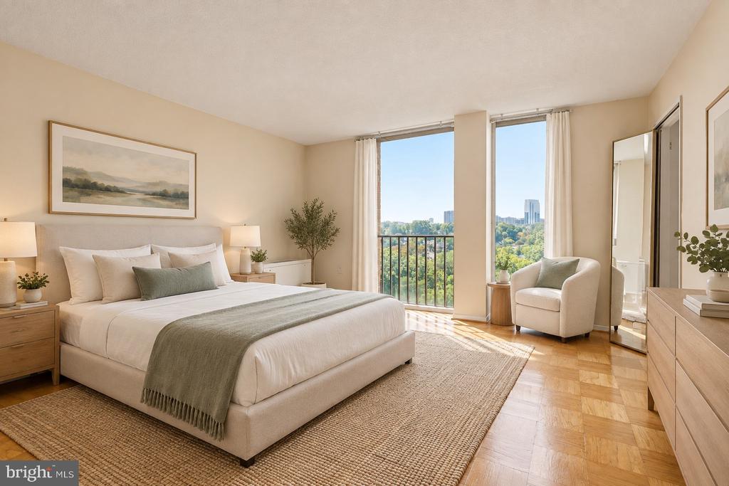 Staged bedroom with a sage-green bed throw and tall windows overlooking treetops and distant buildings.