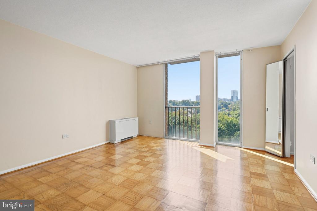 Empty living room with parquet floors and sliding glass doors overlooking trees and distant buildings.