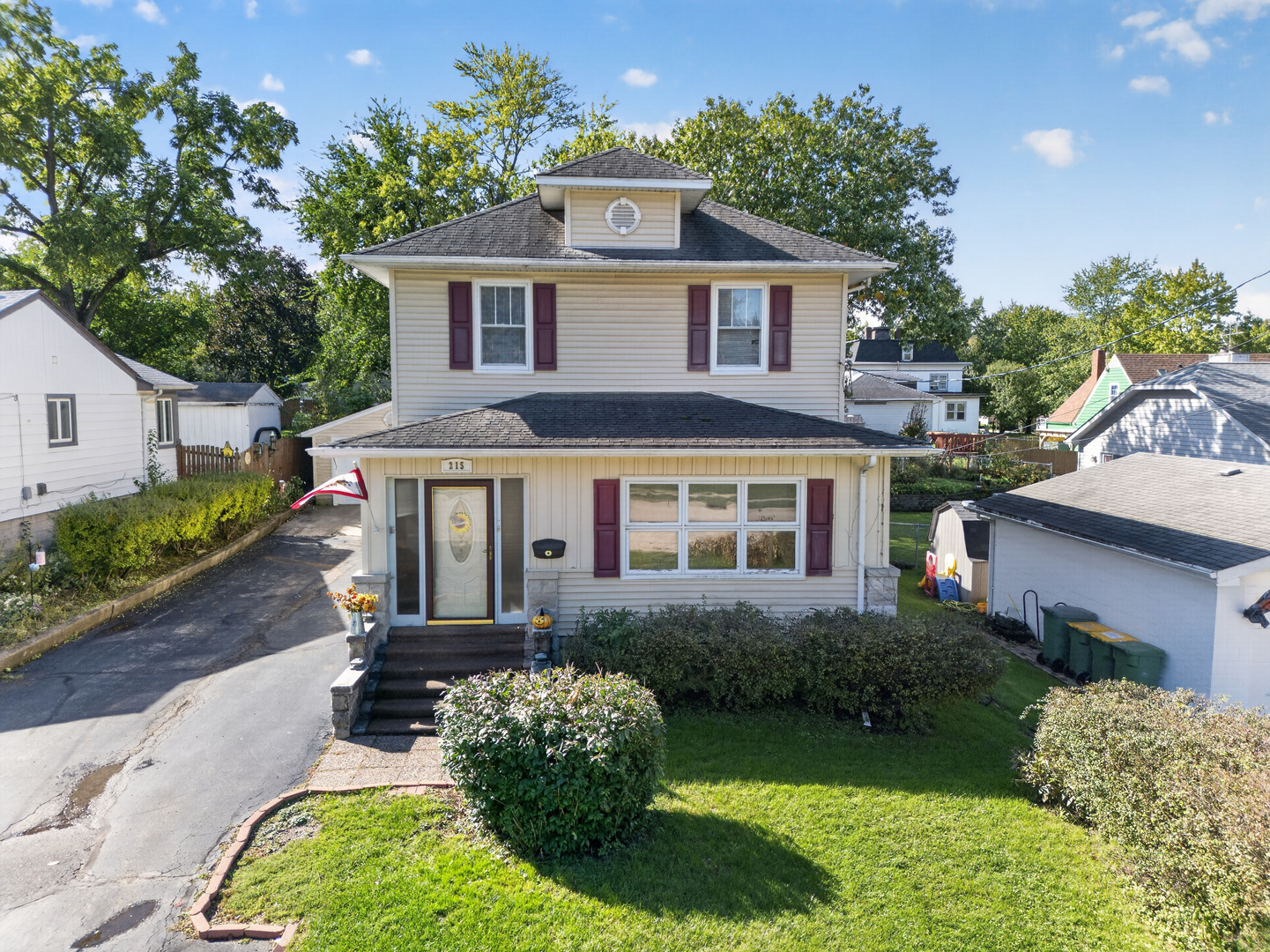 Two-story beige house with burgundy shutters, a cupola, front lawn, and paved driveway.