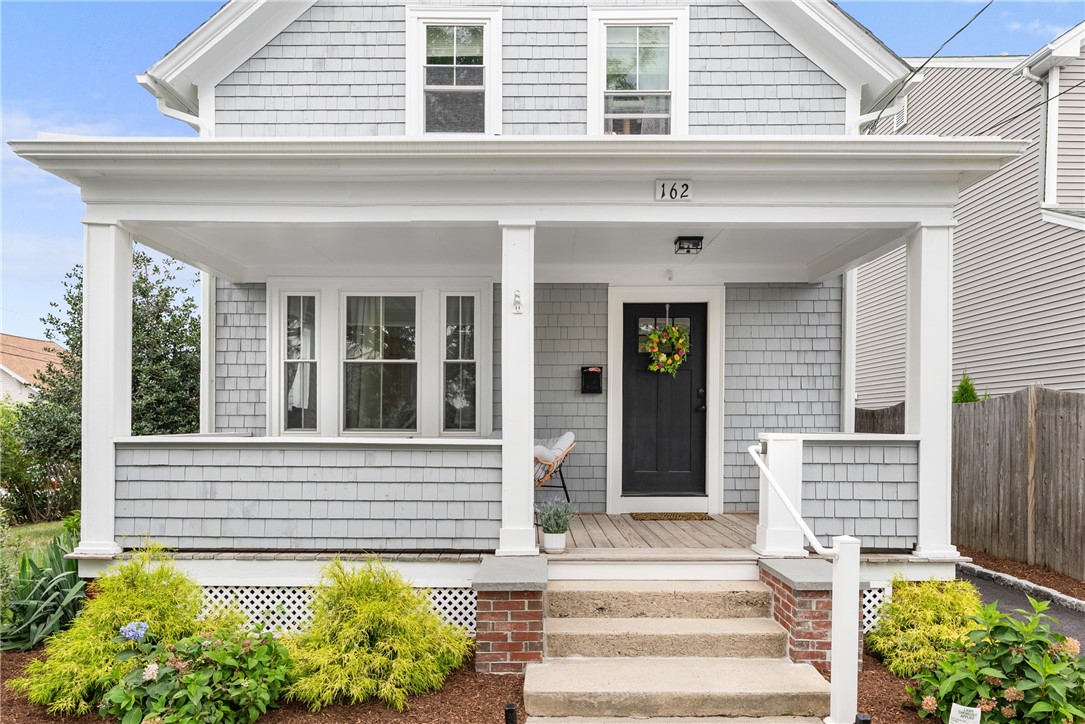 Gray shingle-sided house with a covered front porch, black door, and landscaped entry.