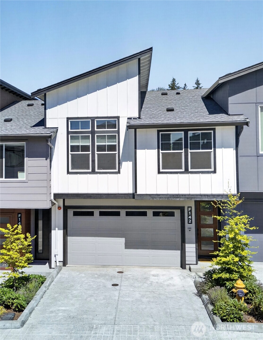 Modern attached home with a steep roof, gray garage, and landscaped driveway.