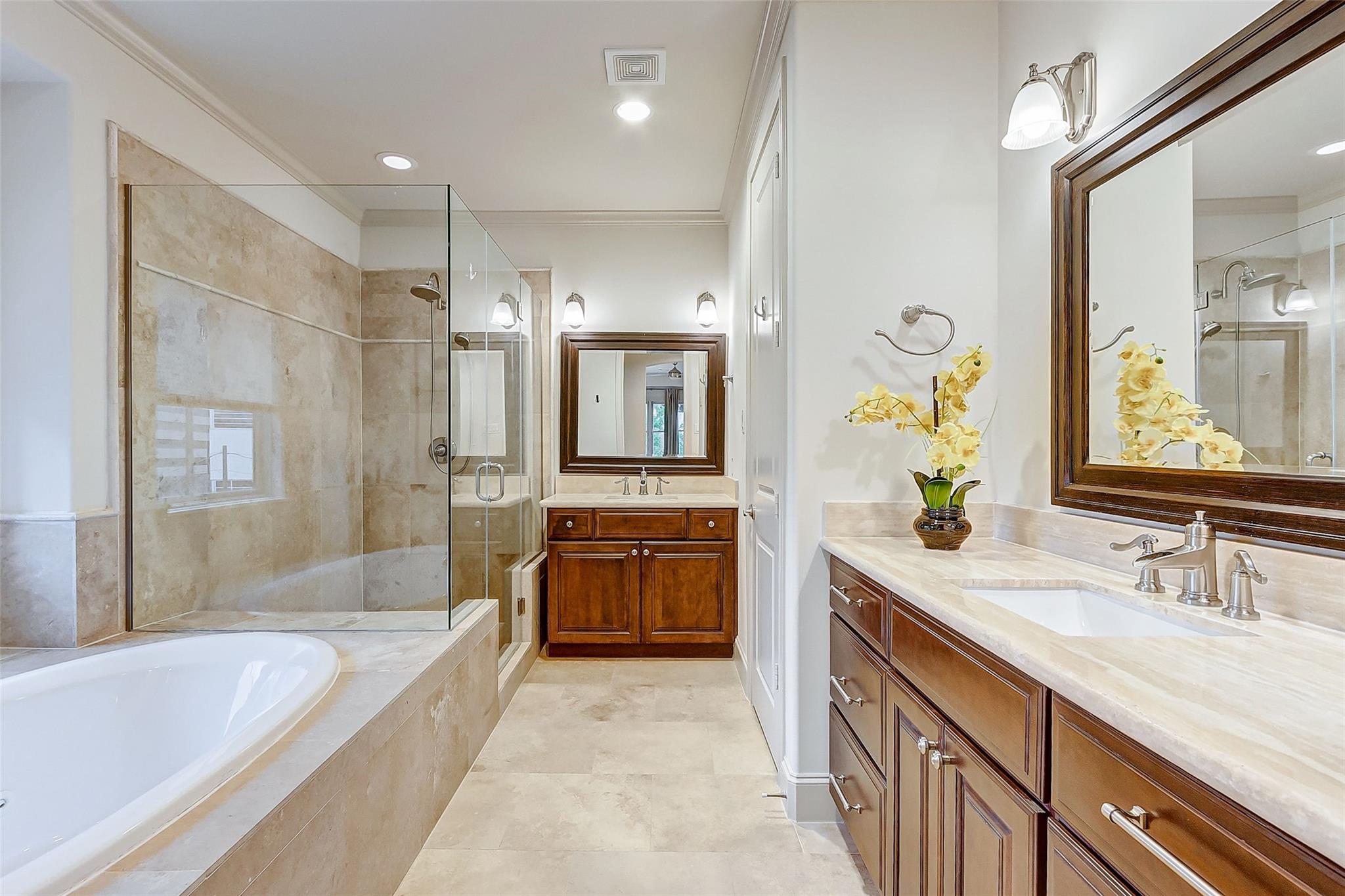 Bathroom with a glass shower, soaking tub, and wood vanities topped with pale stone.