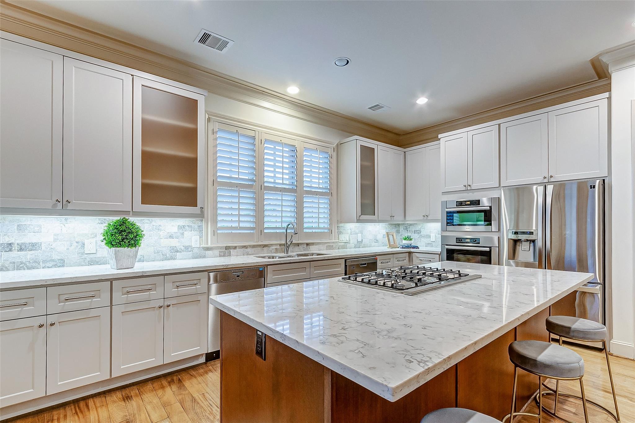 Kitchen with a large cooktop island, white cabinets, stainless steel appliances, and plantation shutters.