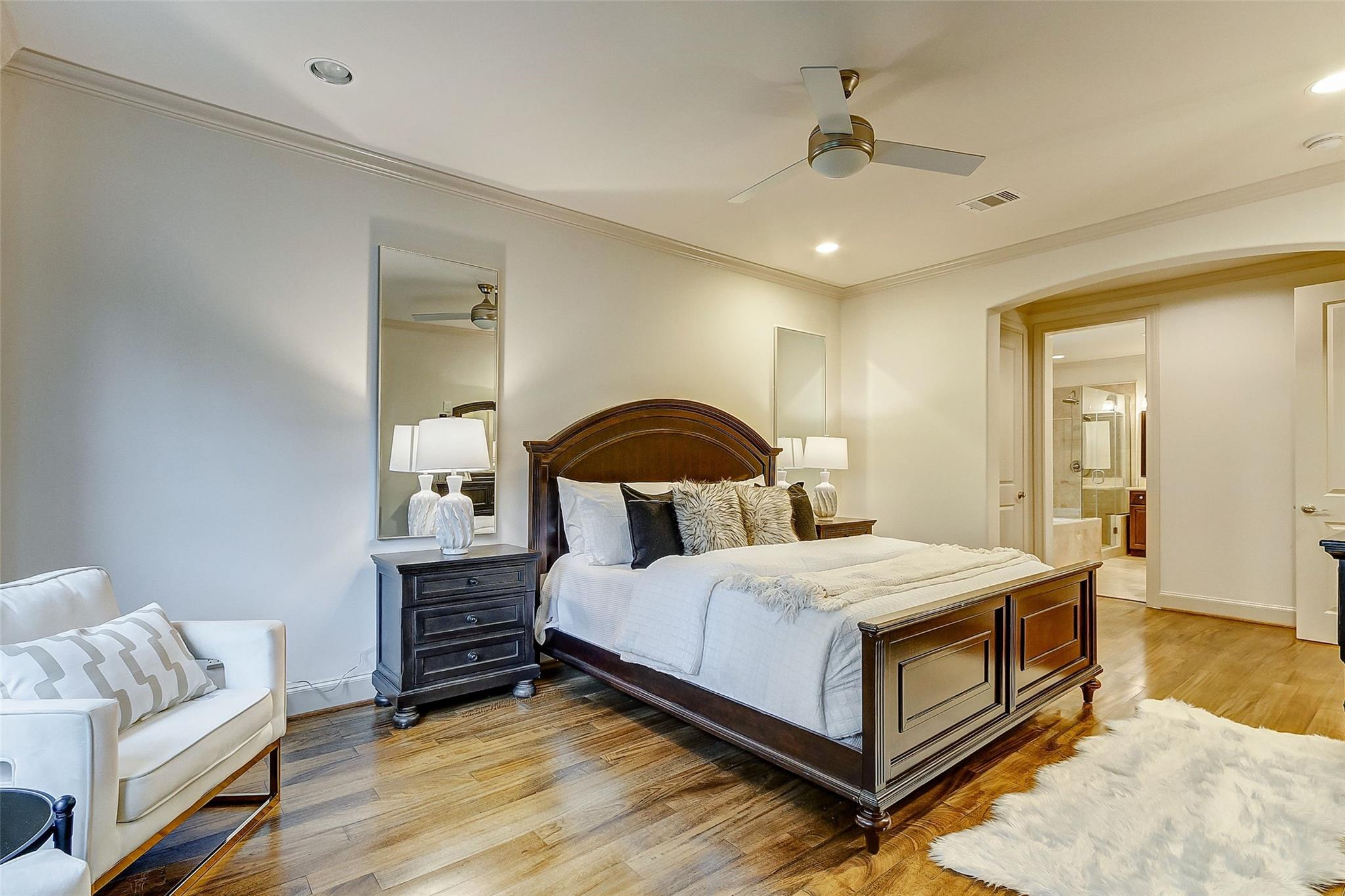Furnished bedroom with a dark wood bed, hardwood floors, and an ensuite bathroom visible through the doorway.