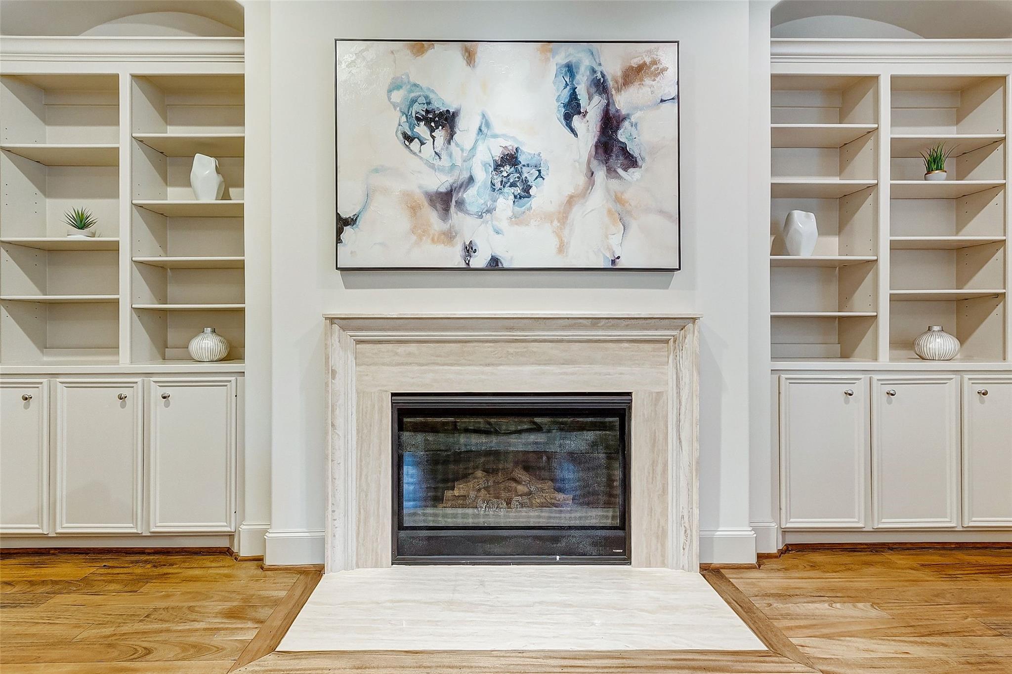 Living room fireplace framed by built-in shelving, with abstract artwork above and wood flooring.