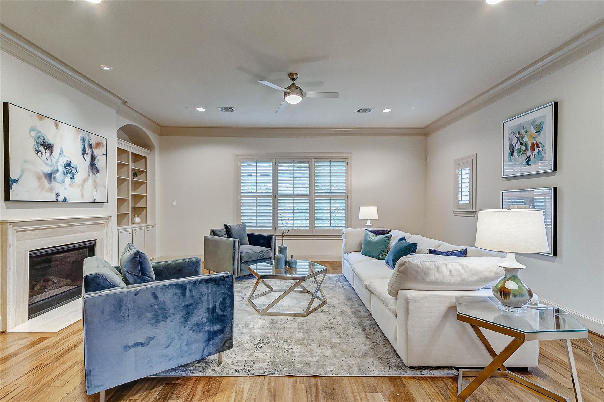 Living room with a fireplace, white sectional, blue accent chairs, and plantation shutters.
