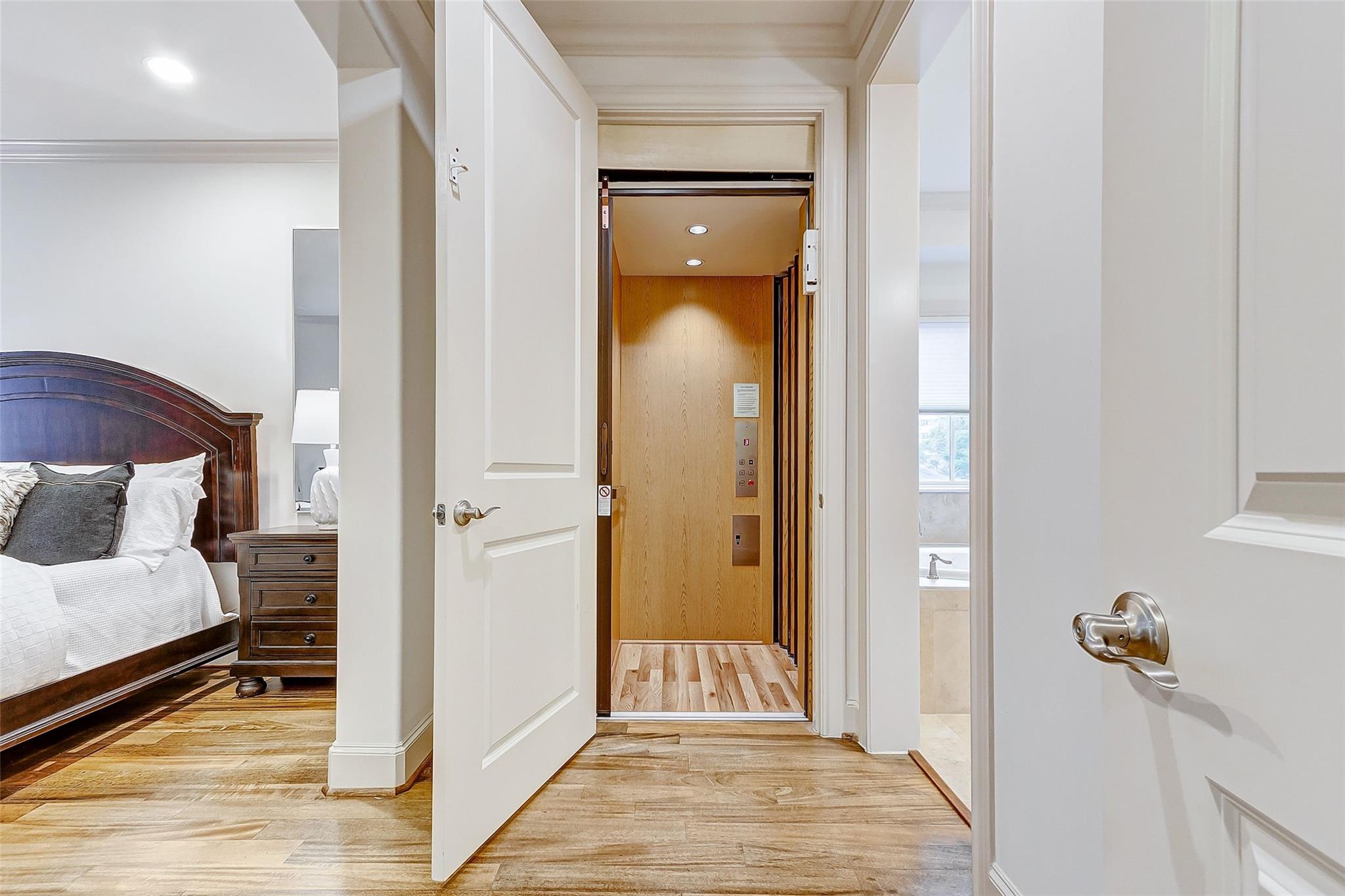 Bedroom with dark wood bed beside an open doorway to a wood-paneled private elevator.