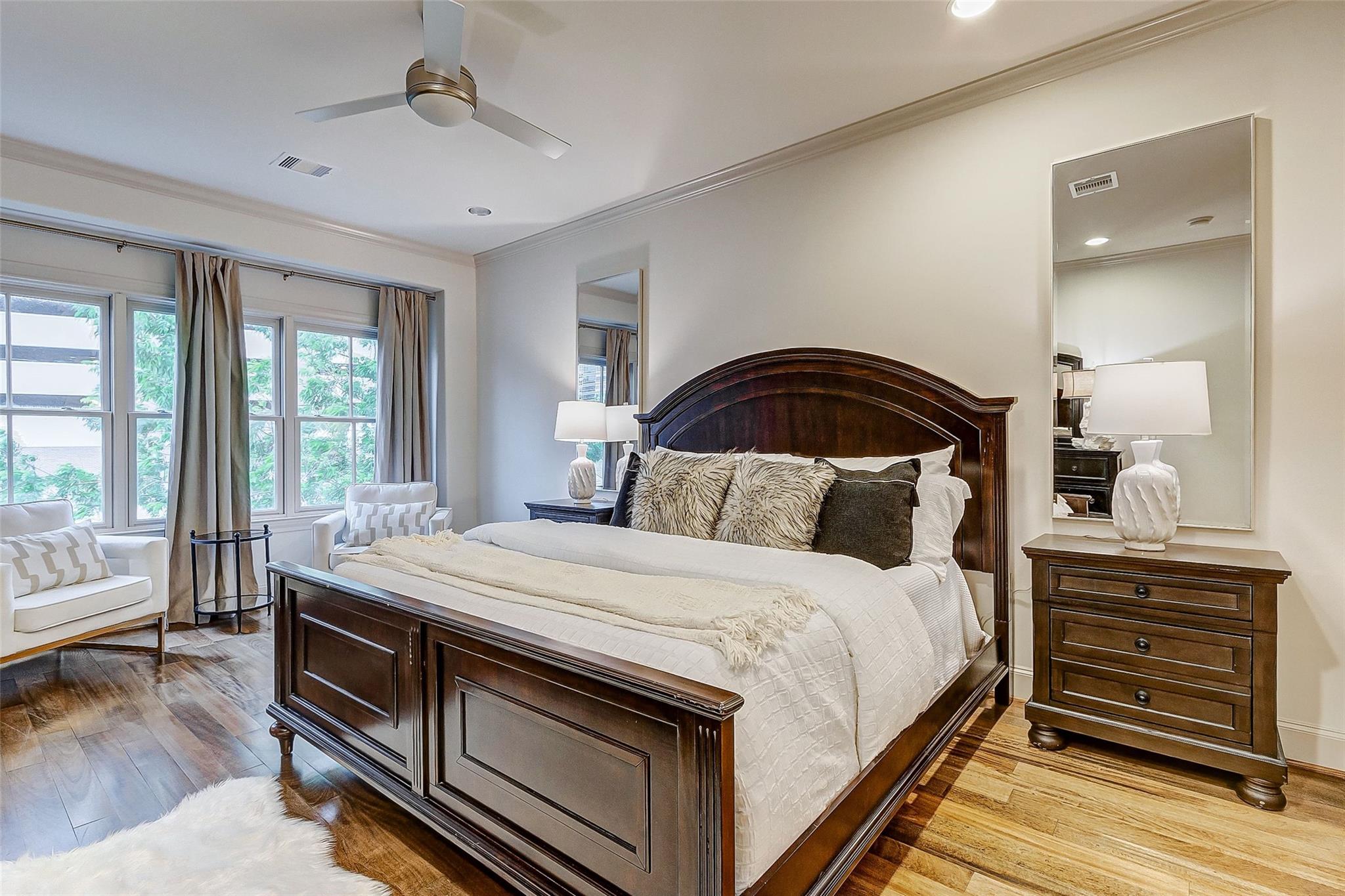 Furnished bedroom with a dark wood bed, tall curtained windows, and wood flooring.