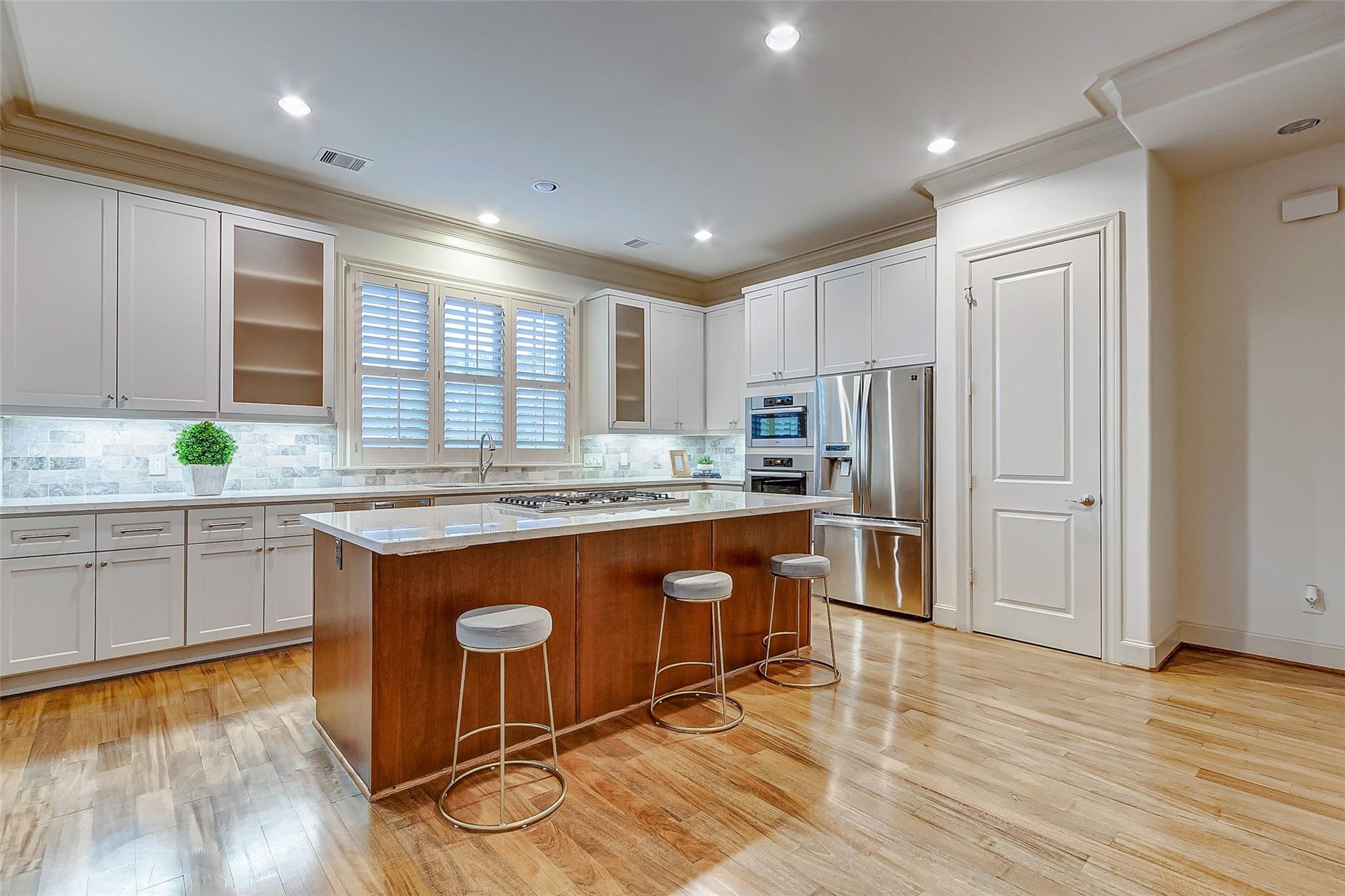 Kitchen with a large wood-paneled island, white cabinetry, and stainless steel appliances.