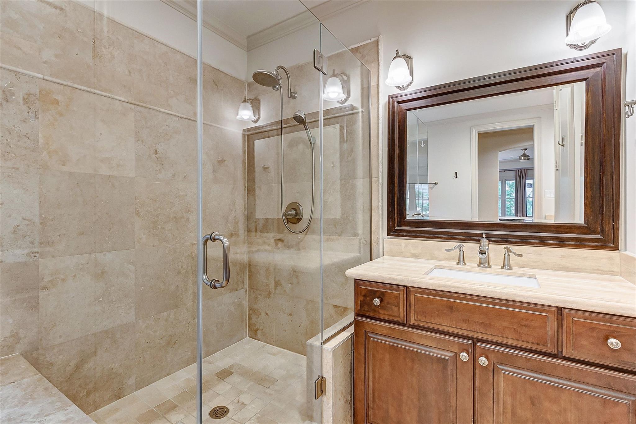 Bathroom with a glass-enclosed stone-tiled shower and dark wood vanity beneath a large framed mirror.