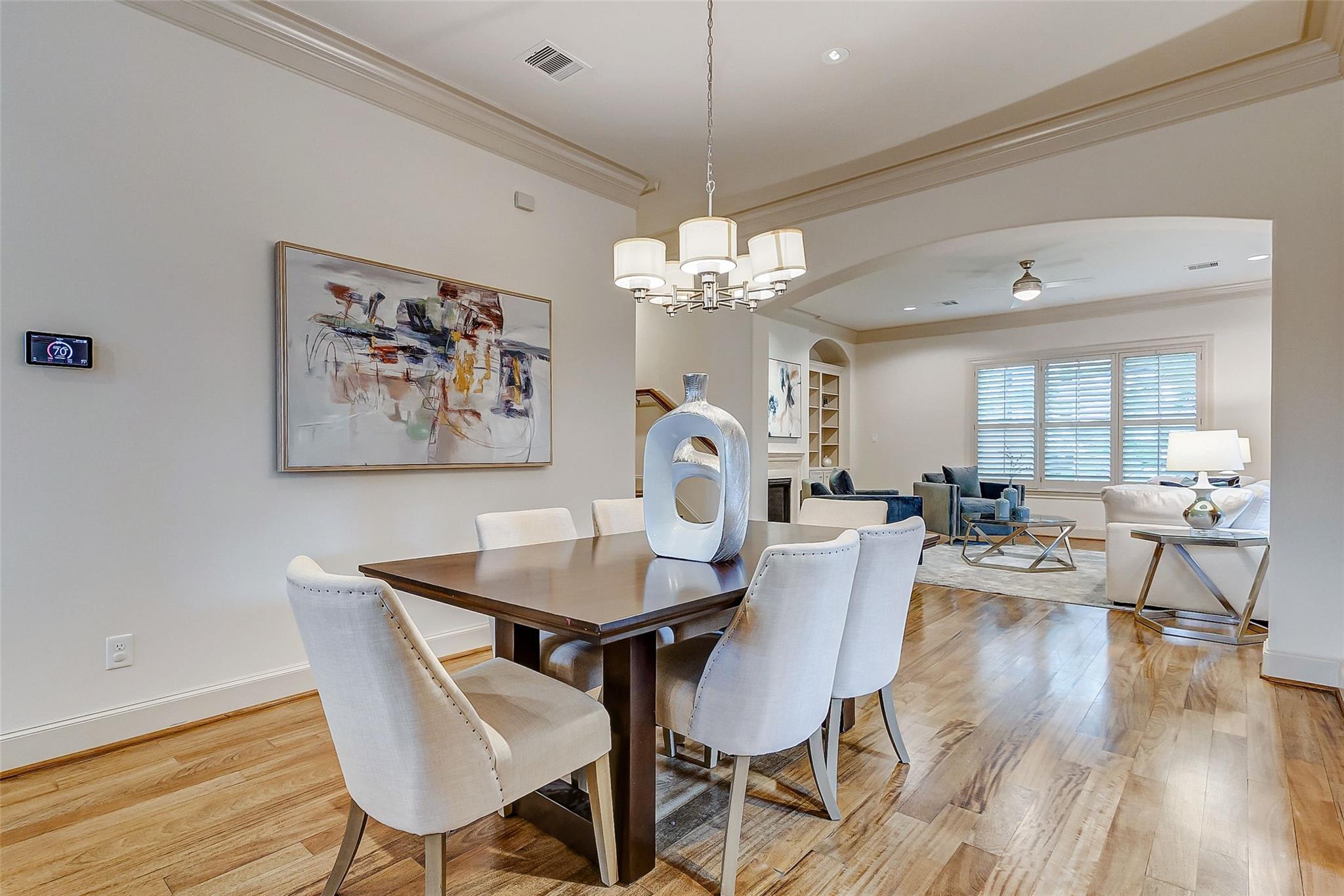 Dining room with a dark wood table and chandelier, opening onto a living room with shuttered windows.