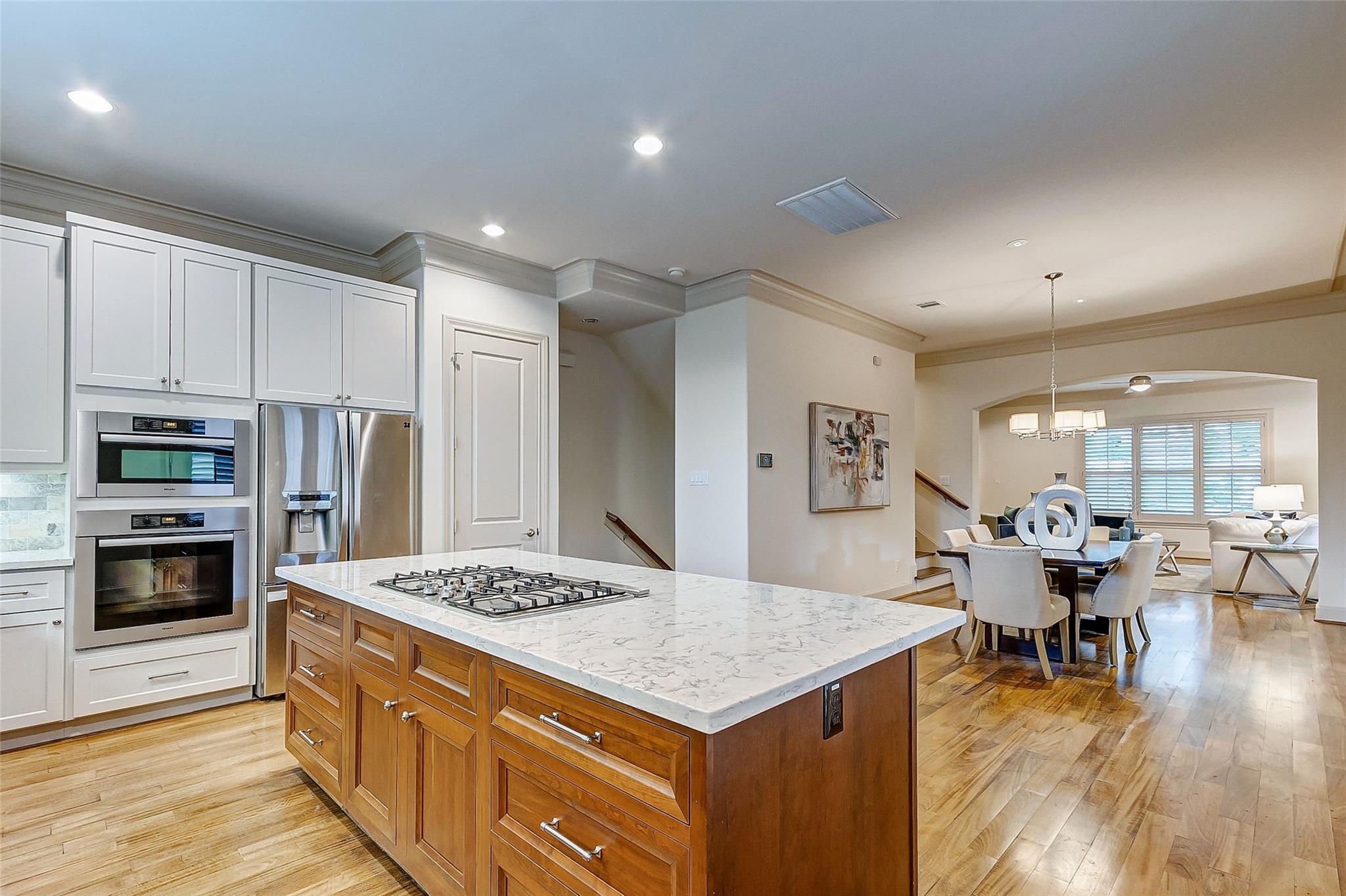 Kitchen with a large marble-topped island, gas cooktop, white cabinets, and adjoining dining area.