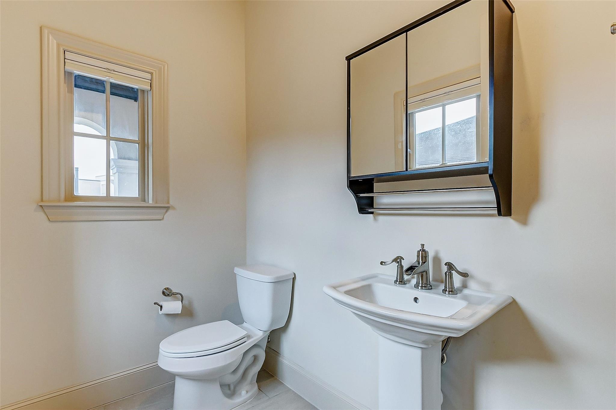 Bathroom with a pedestal sink beneath a large mirrored cabinet and a white-trimmed window.