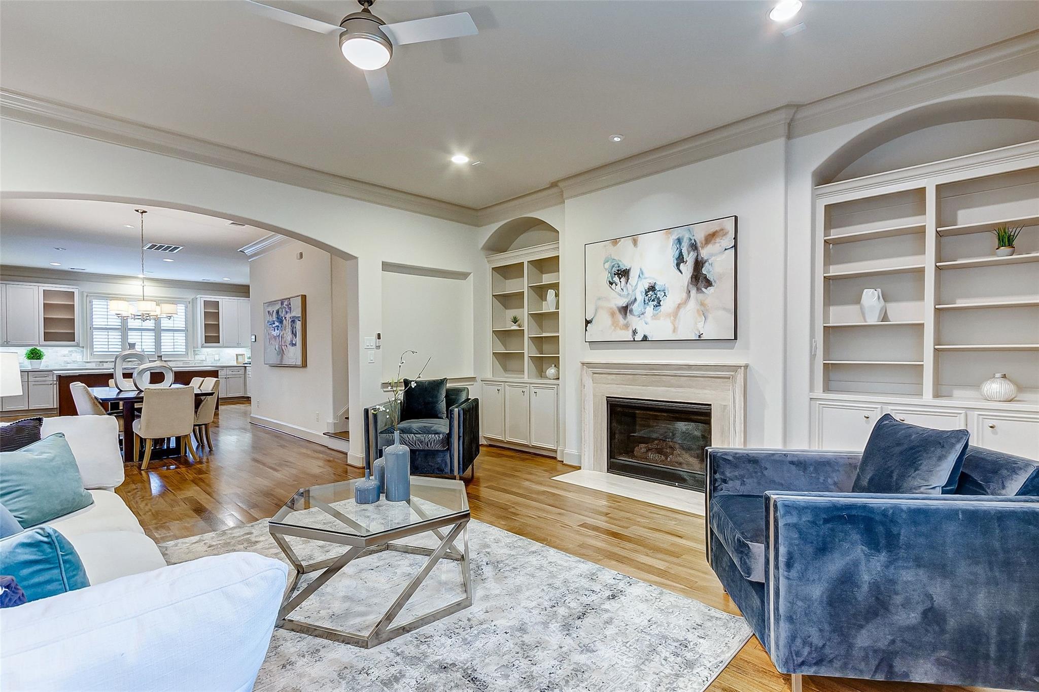 Living room with a fireplace, built-in shelves, blue chairs, and an adjoining dining area and kitchen.