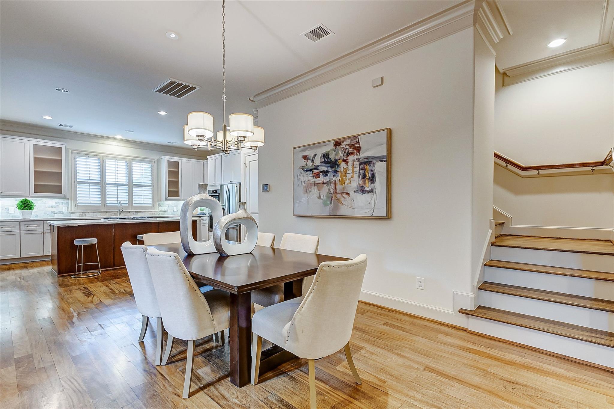 Dining room with a dark wood table, white chairs, hardwood floors, and an adjoining kitchen and staircase.