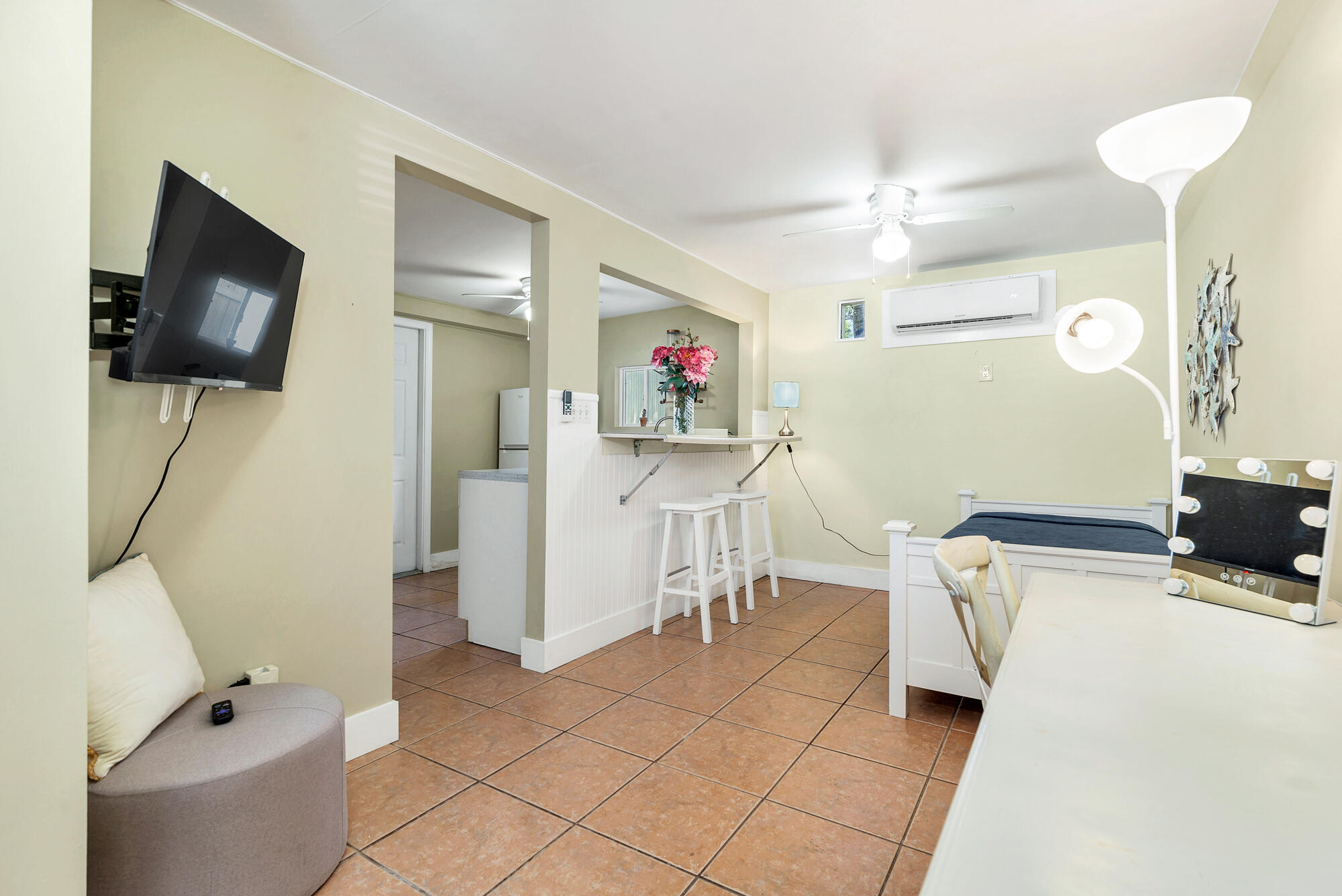 Furnished bedroom with a small kitchenette, terracotta tile floors, and a wall-mounted television.
