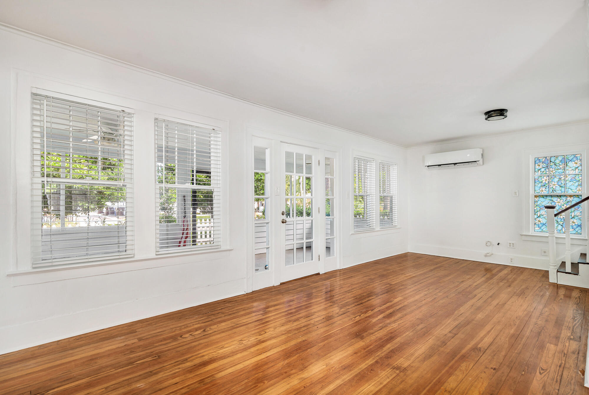 Empty room with polished hardwood floors, French doors, and a colorful stained-glass window.