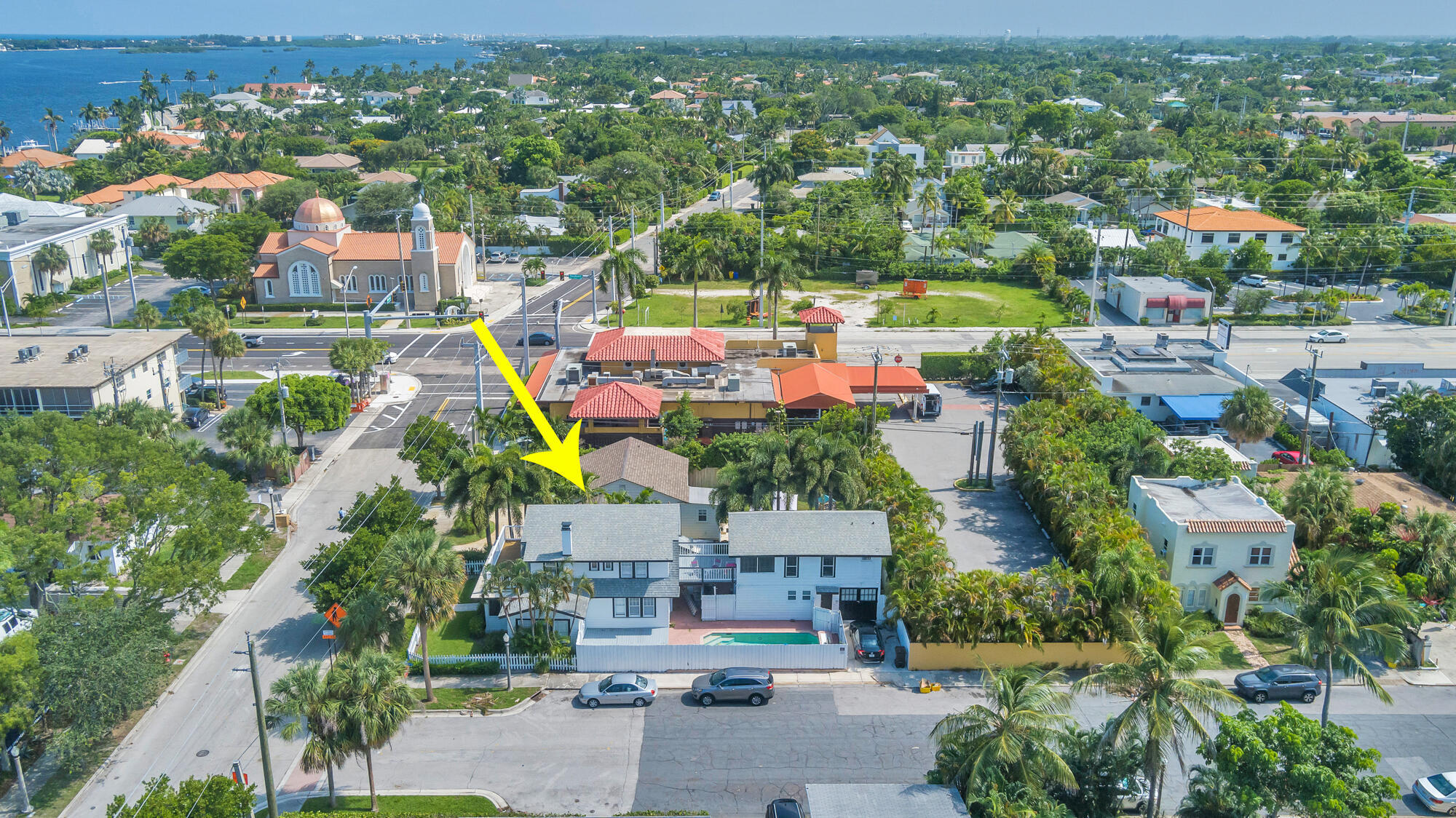 Aerial view of a home marked by a yellow arrow, with palm trees and water in the distance.