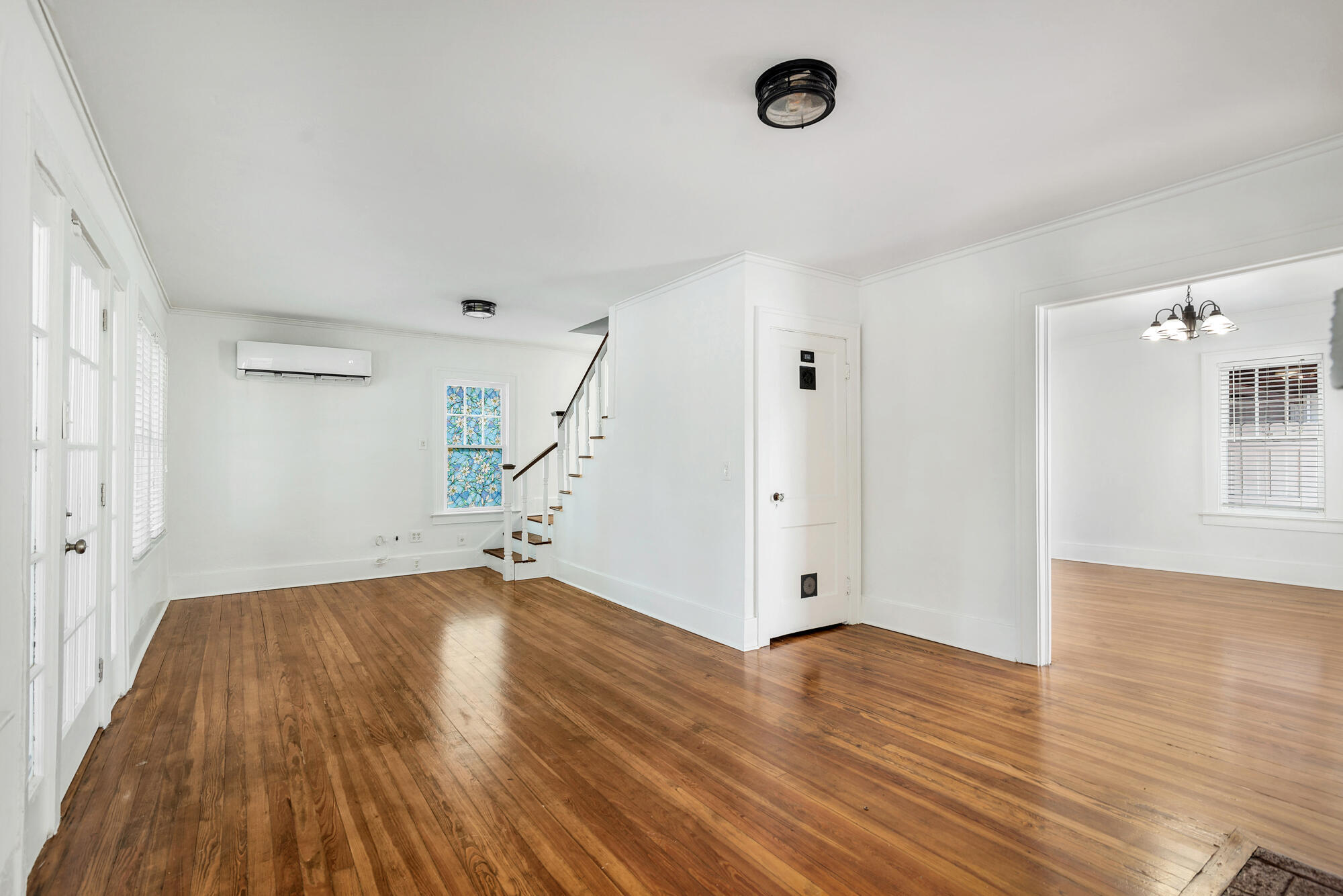 Empty white living area with polished hardwood floors, a staircase, and a colorful stained-glass window.