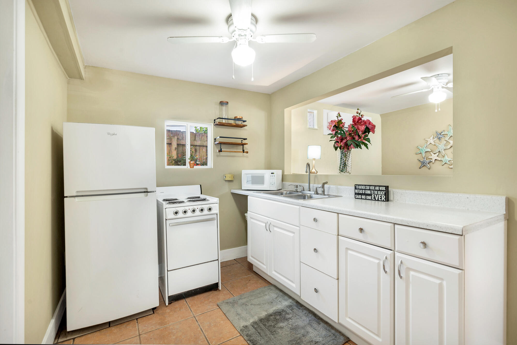 Kitchen with white cabinets, white appliances, and a pass-through to a room decorated with flowers and starfish.