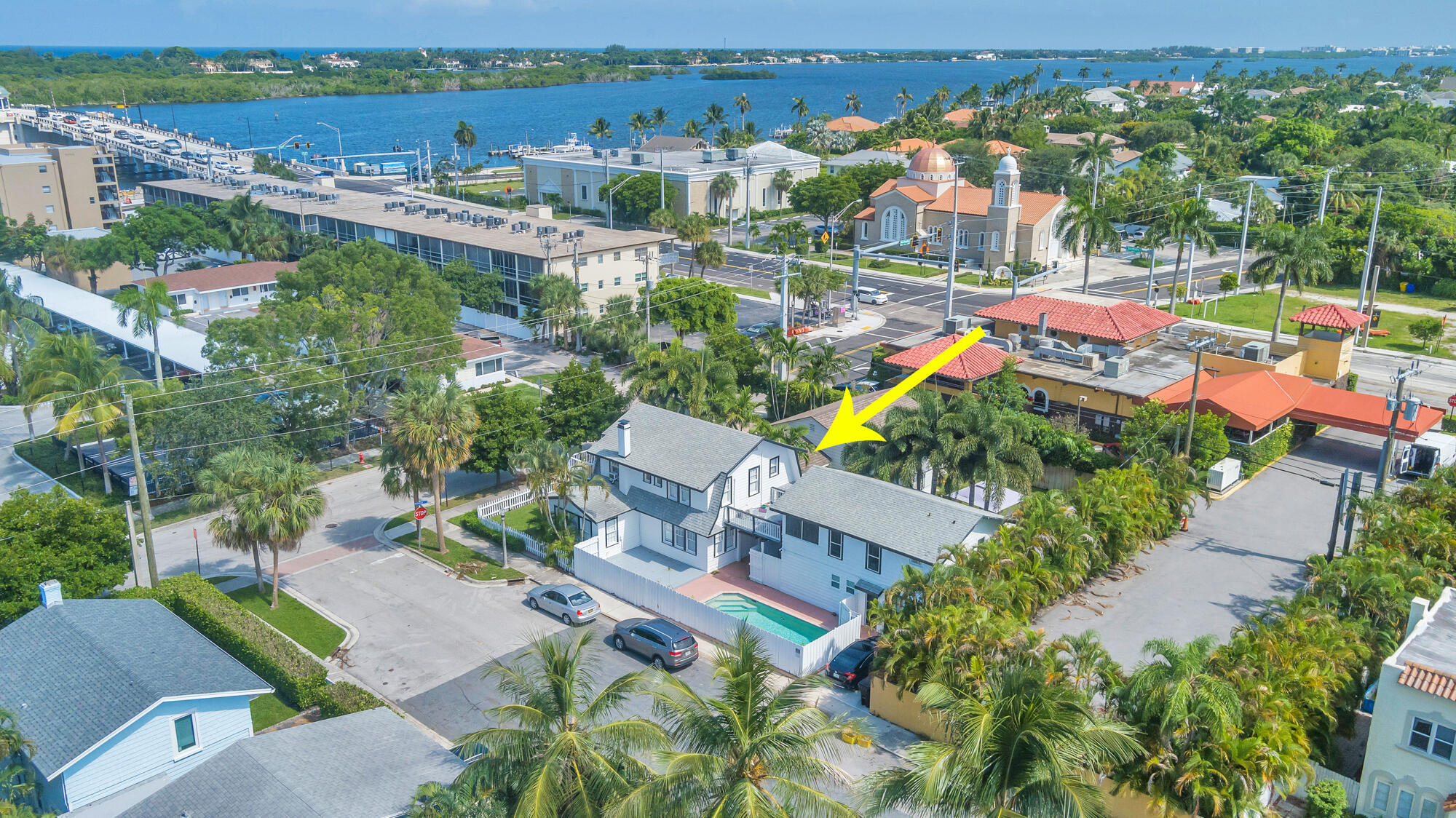 Aerial view of the white property and pool, with a bridge and broad waterway beyond.