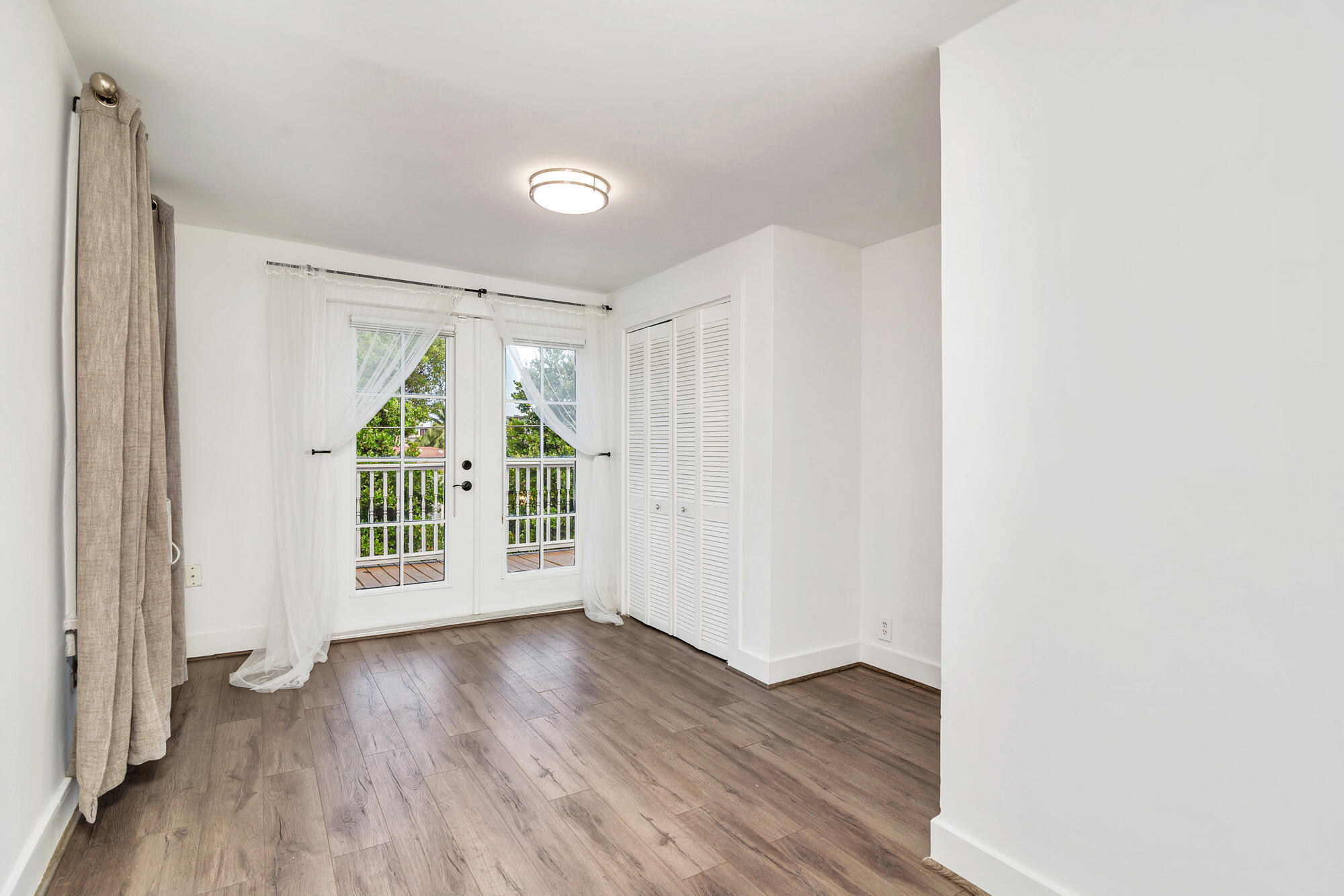 Unfurnished bedroom with wood-look floors, louvered closet doors, and French doors to a balcony.