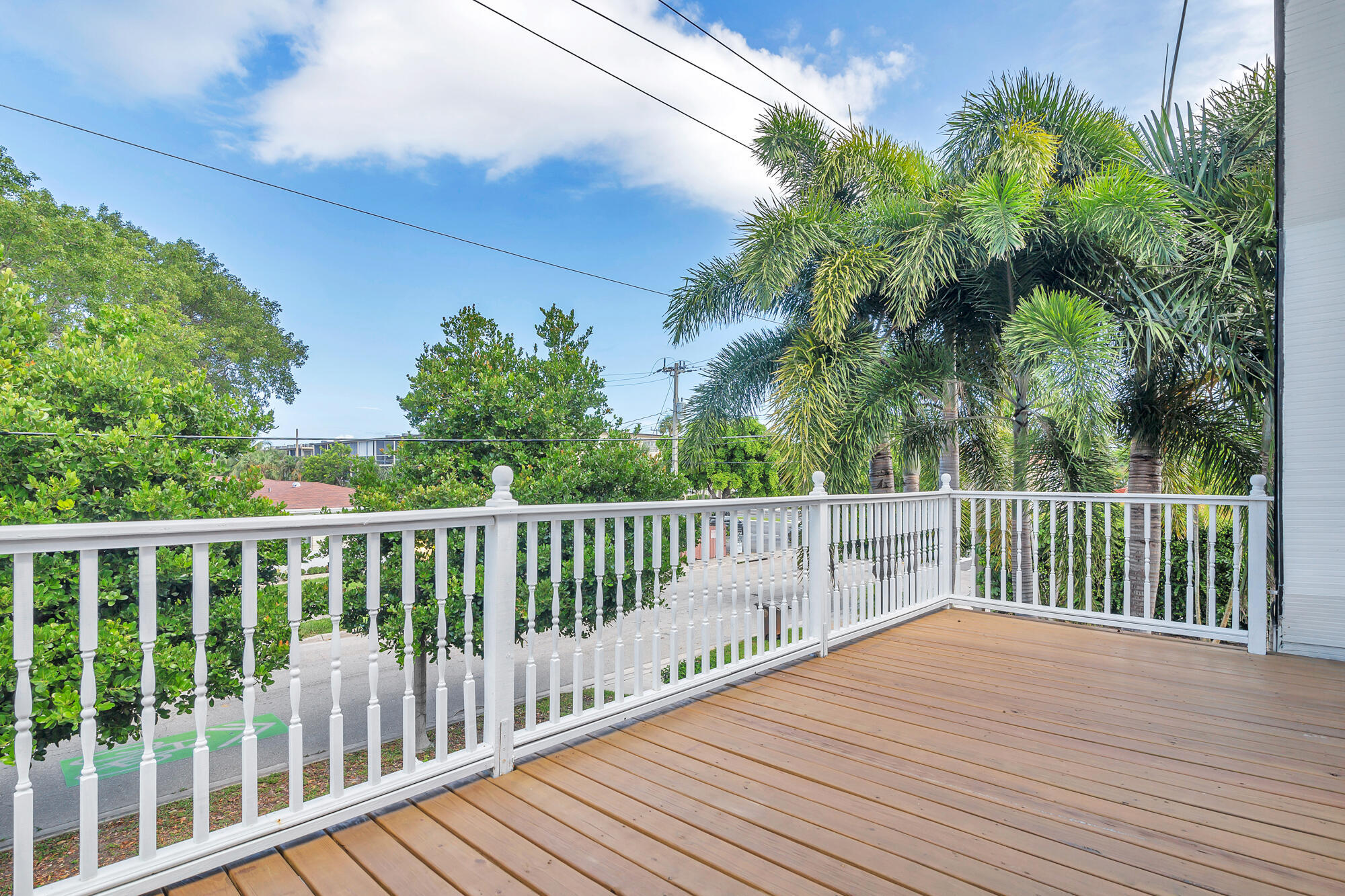 Wood-plank deck with white railings overlooking palm trees and greenery.