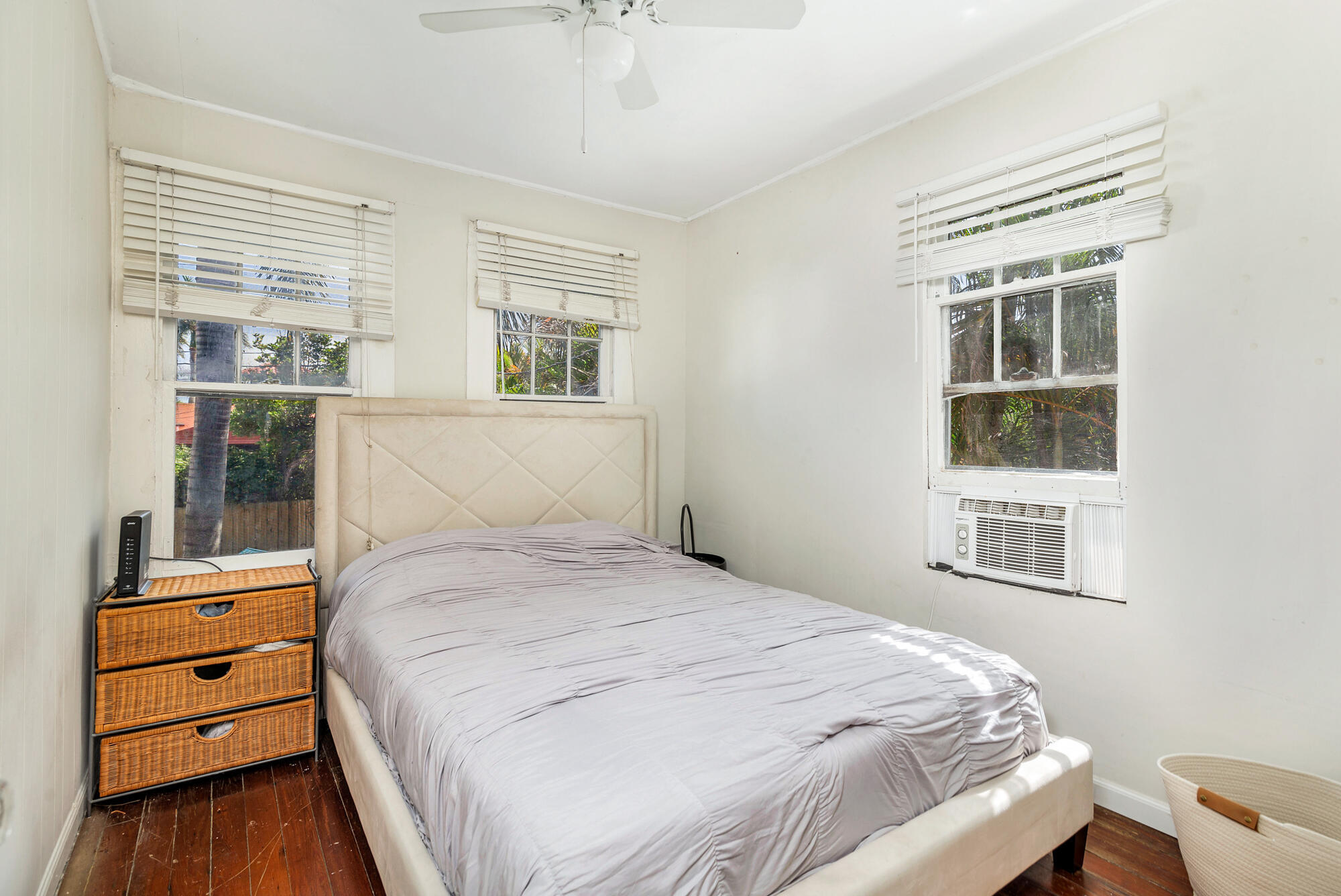 Bedroom with a large bed, hardwood floors, three windows, and a window air conditioner.