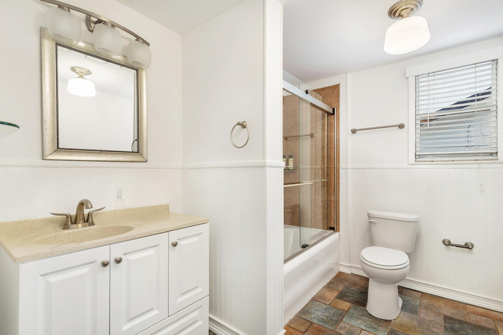 Bathroom with a glass-enclosed tiled shower, white vanity, and multicolored floor tiles.