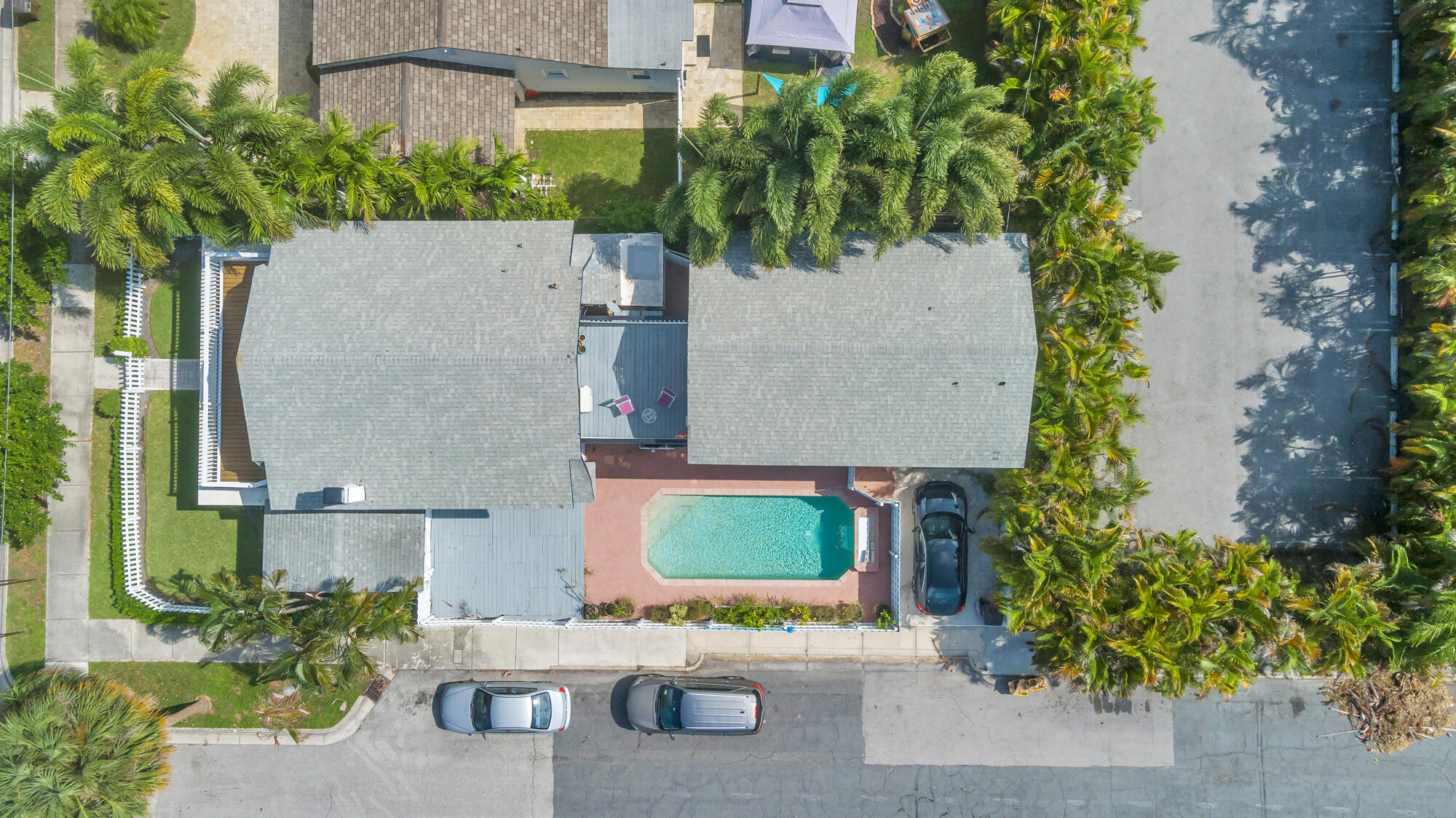 Aerial view of a palm-lined house with a backyard swimming pool and fenced lawn.