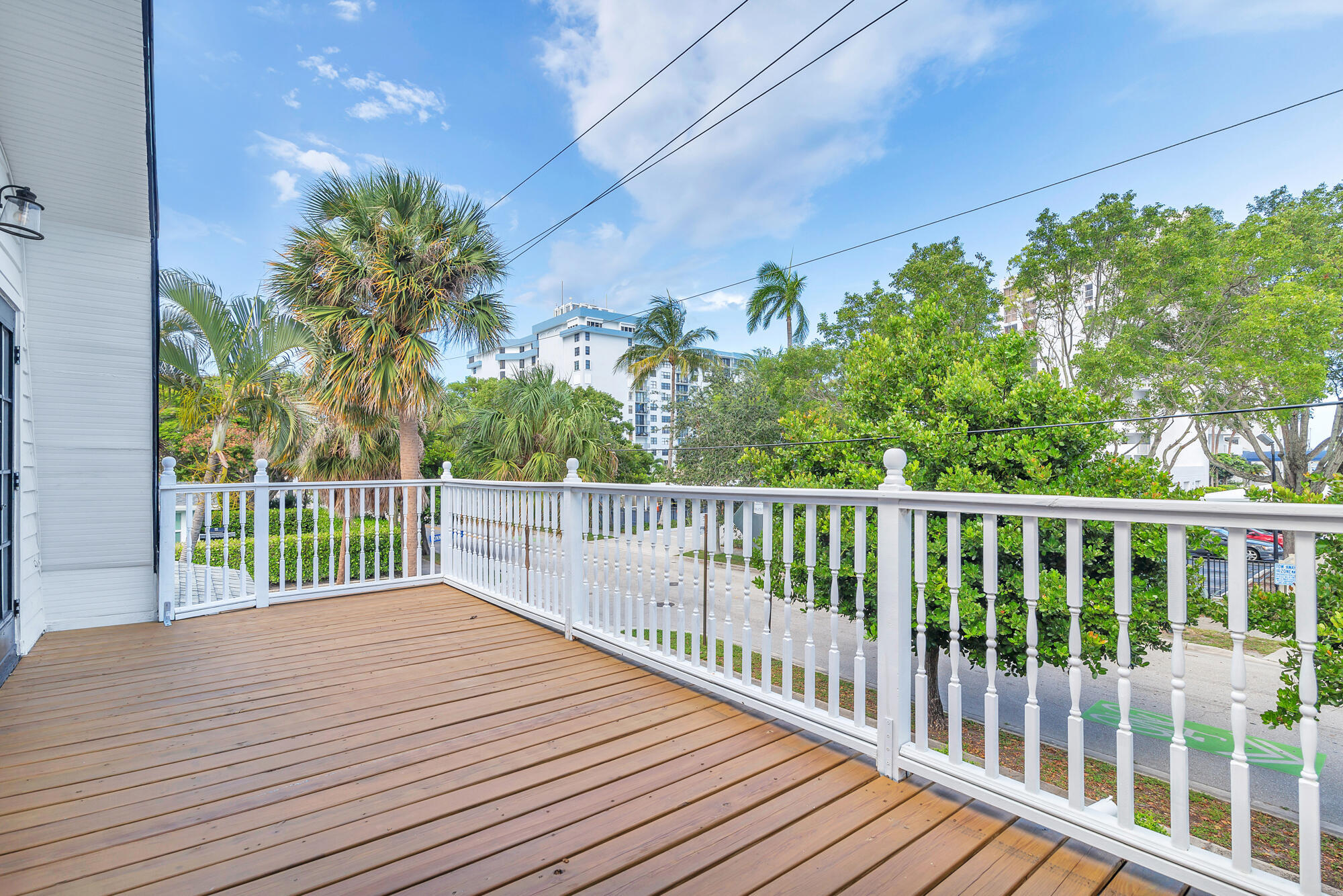 Elevated wooden deck with white railings, palm trees, and nearby buildings beyond.