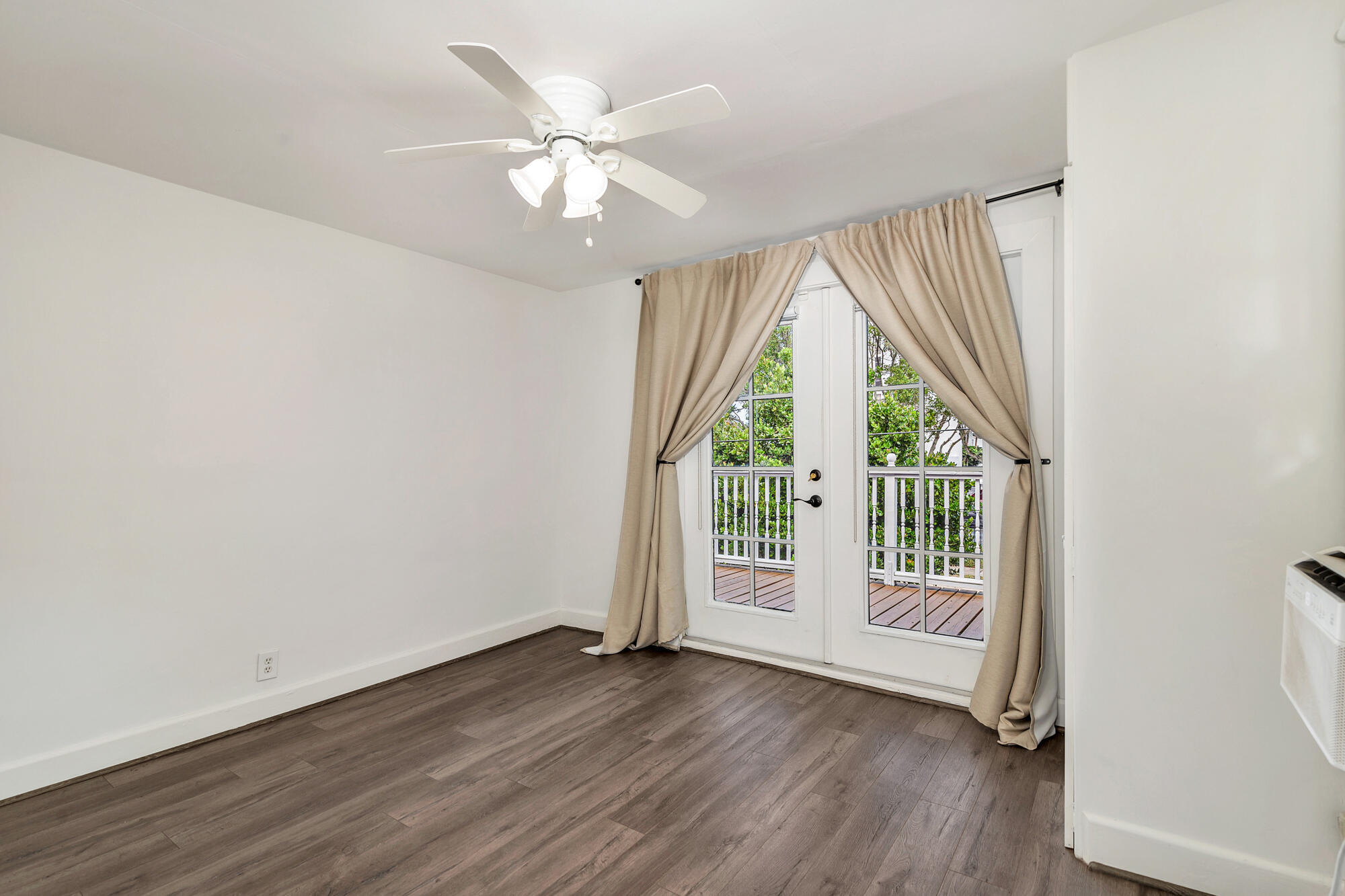 Empty room with dark flooring, a ceiling fan, and curtained French doors to a balcony.