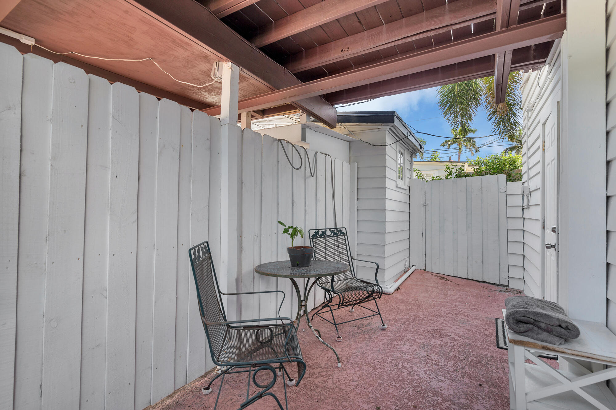 Covered patio with white privacy fencing, pink concrete floor, and black metal table and chairs.