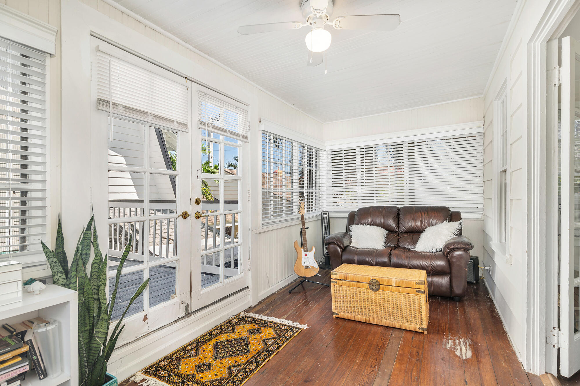 Sunroom with French doors to a deck, leather loveseat, guitar, and wicker chest.
