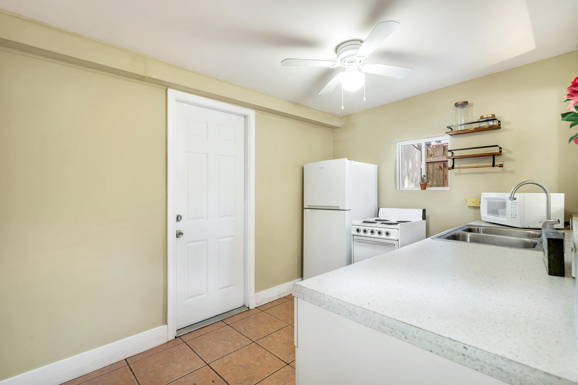Compact kitchen with white refrigerator and stove, double sink, and terracotta tile floor.