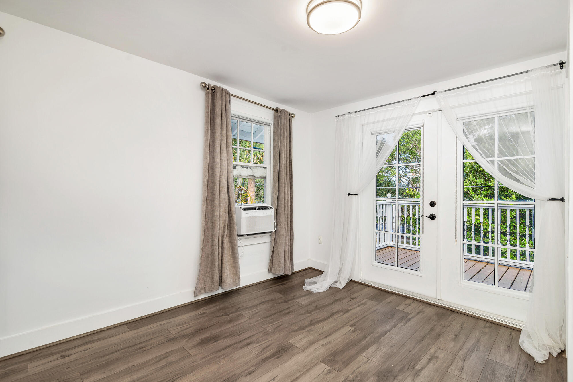 Unfurnished room with wood-look floors, a window air conditioner, and French doors to a leafy balcony.