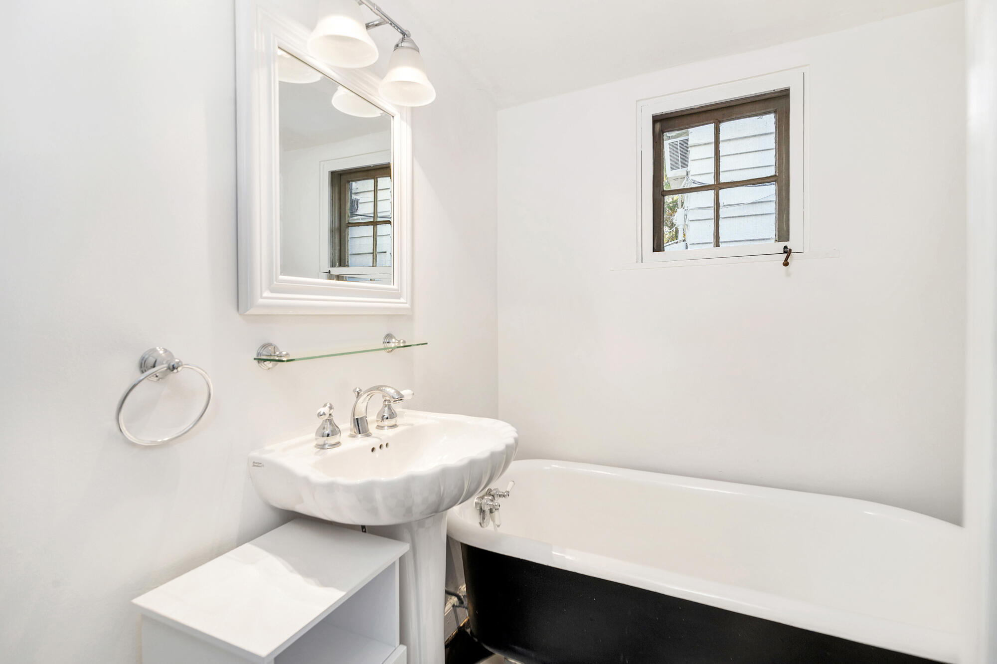 Bathroom with a pedestal sink and mirror beside a white tub with a black exterior.