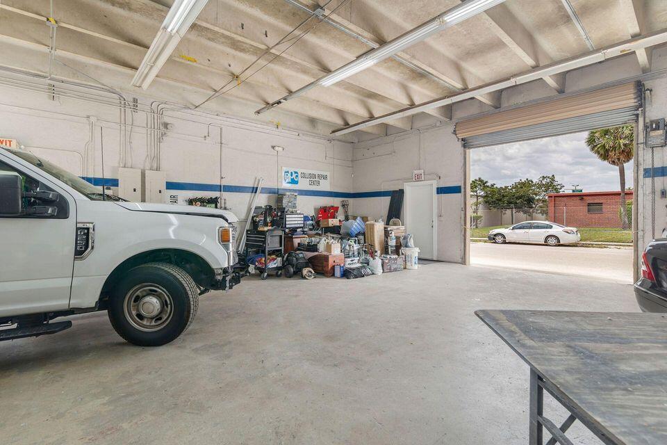Vehicle repair garage with an open roll-up door, white pickup, and workshop equipment.