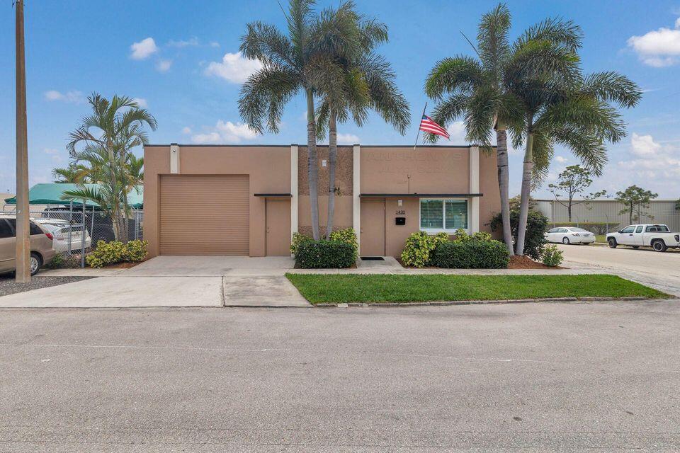 Tan commercial building with a roll-up garage door, palm trees, and an American flag.