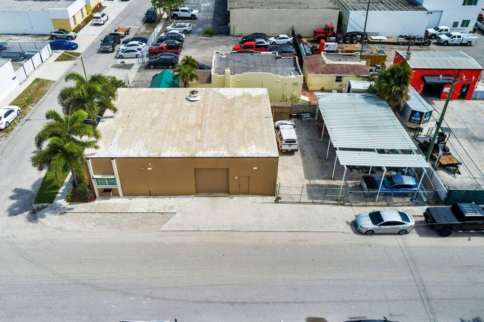 Commercial building with a flat roof, palm trees, and covered vehicle parking, viewed from above.